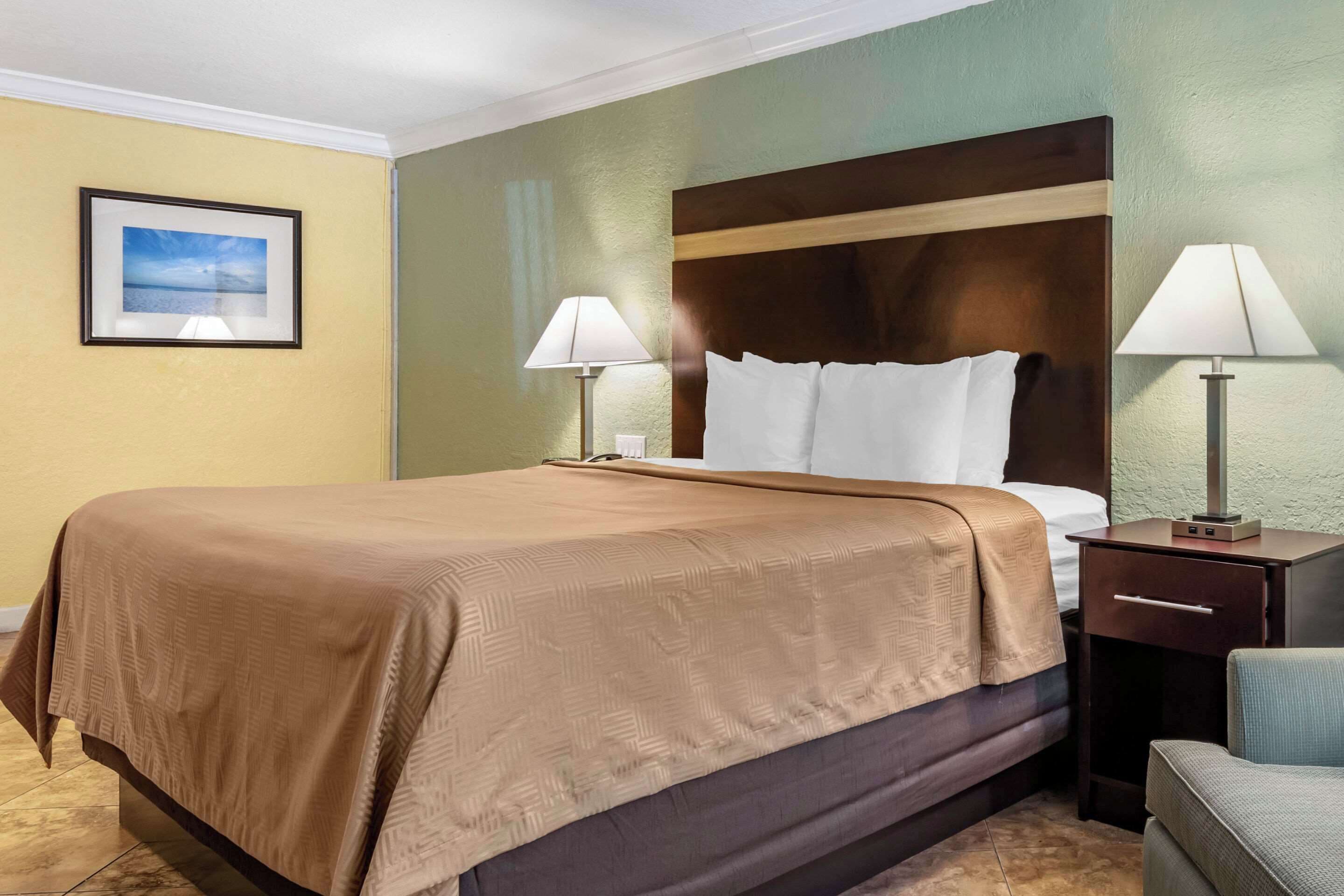 A hotel room with a large bed, two bedside tables with lamps, a chair, and a framed picture on the wall.