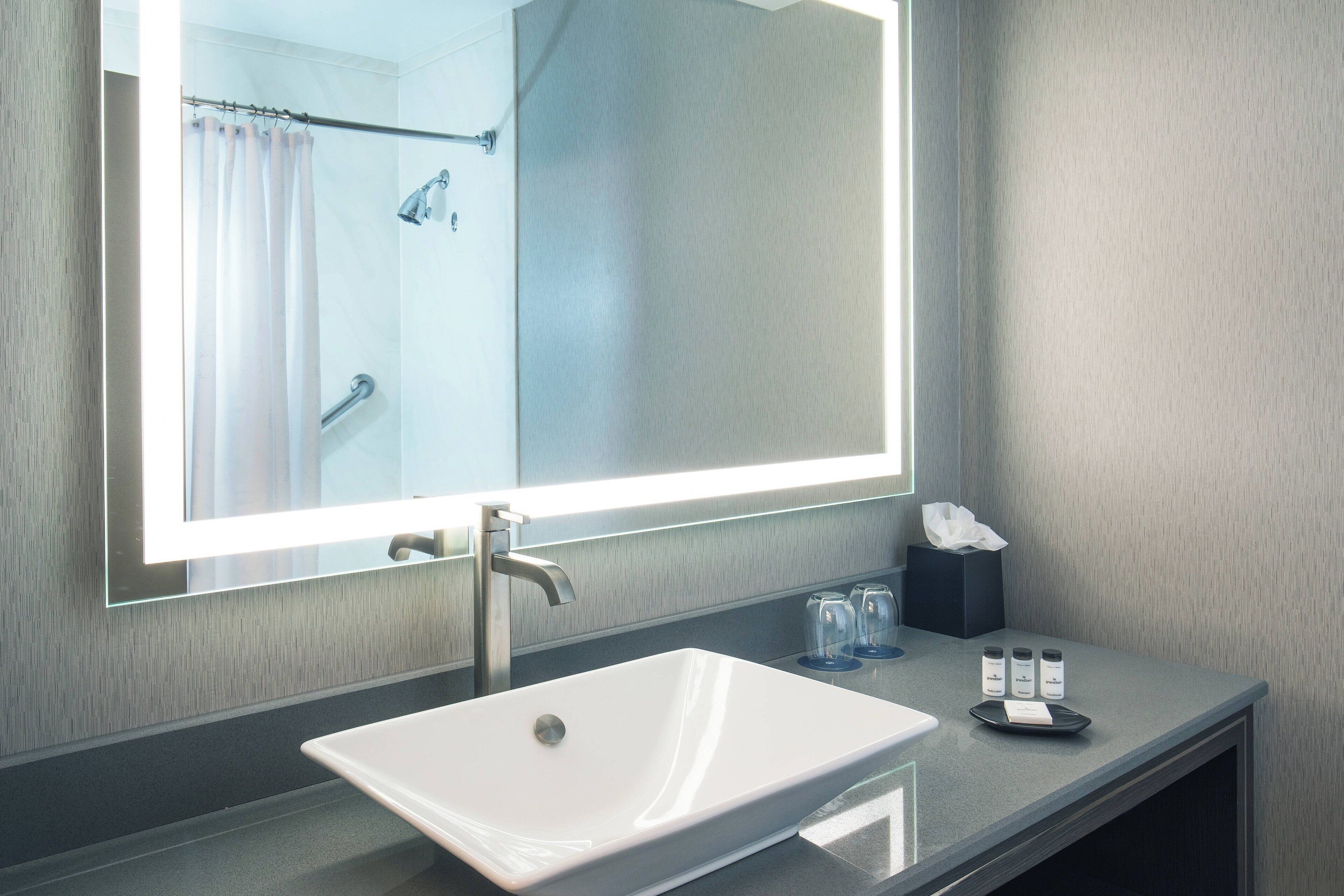 A modern bathroom with a large mirror, a white sink, and a shower area.