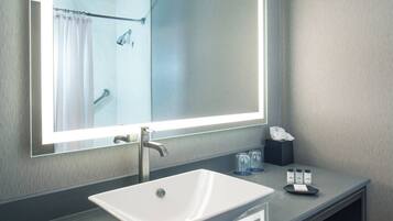 A modern bathroom with a large mirror, a white sink, and a shower area.