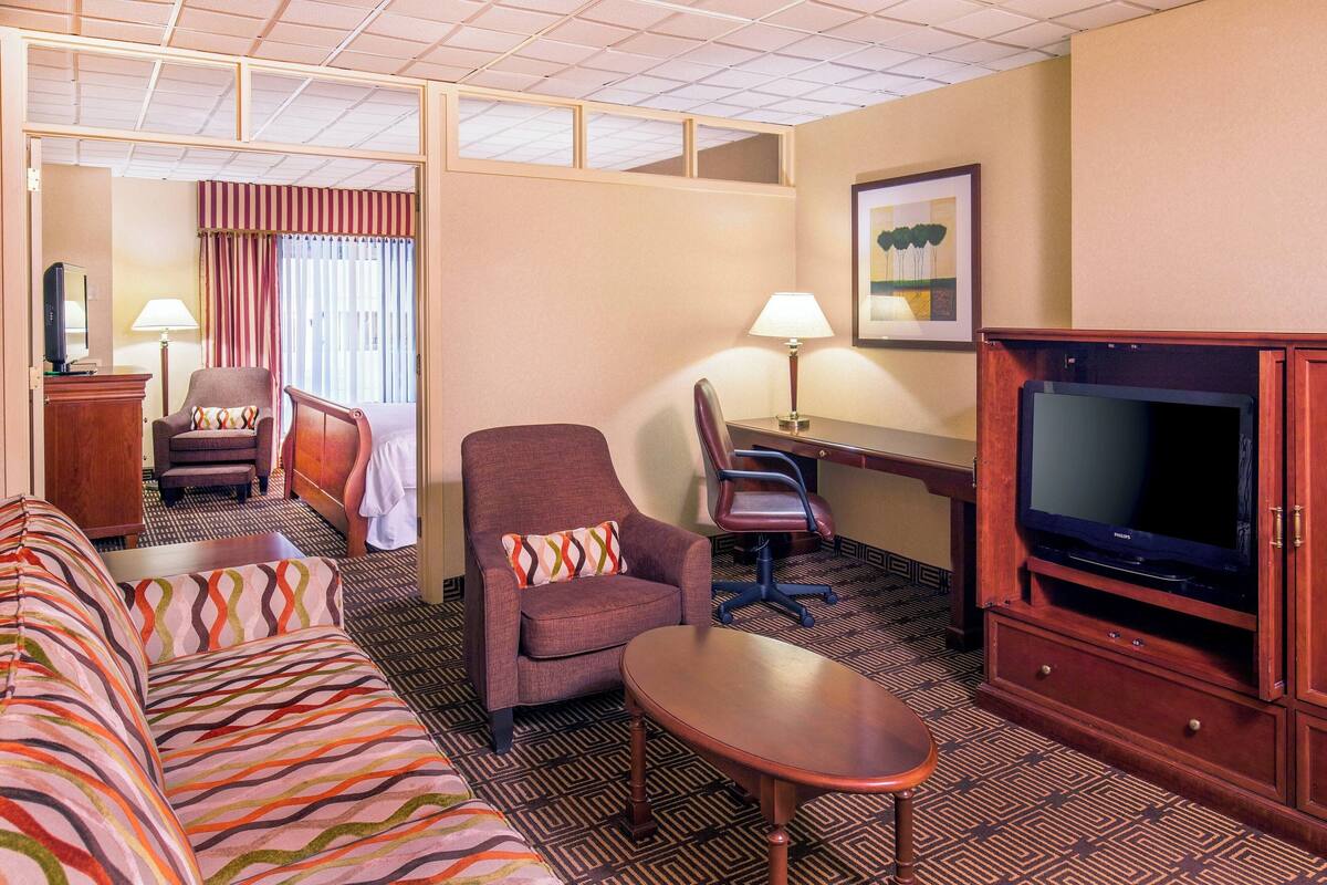 A hotel room with a sofa, two armchairs, a desk, a television, and a lamp.