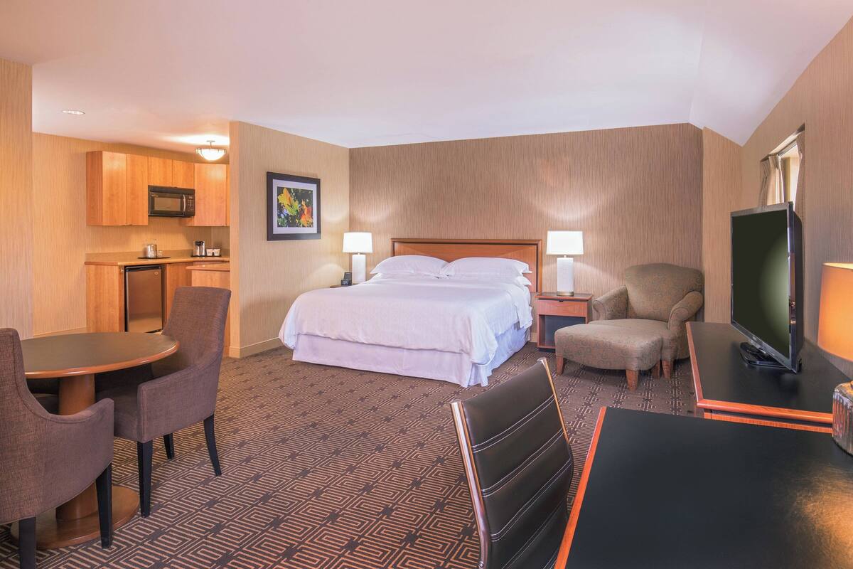 A hotel room with a bed, a desk, a chair, a television, and a microwave.