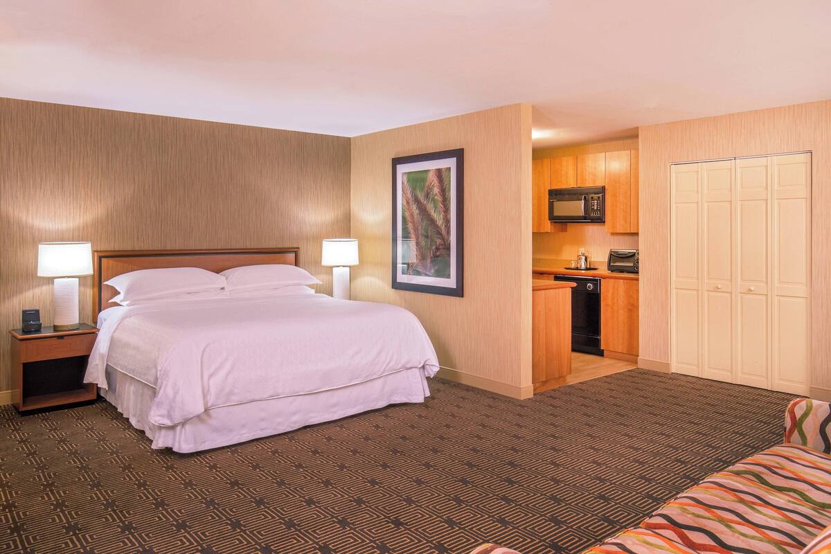 A hotel room with a bed, bedside tables, a desk, a kitchenette, and a wardrobe.