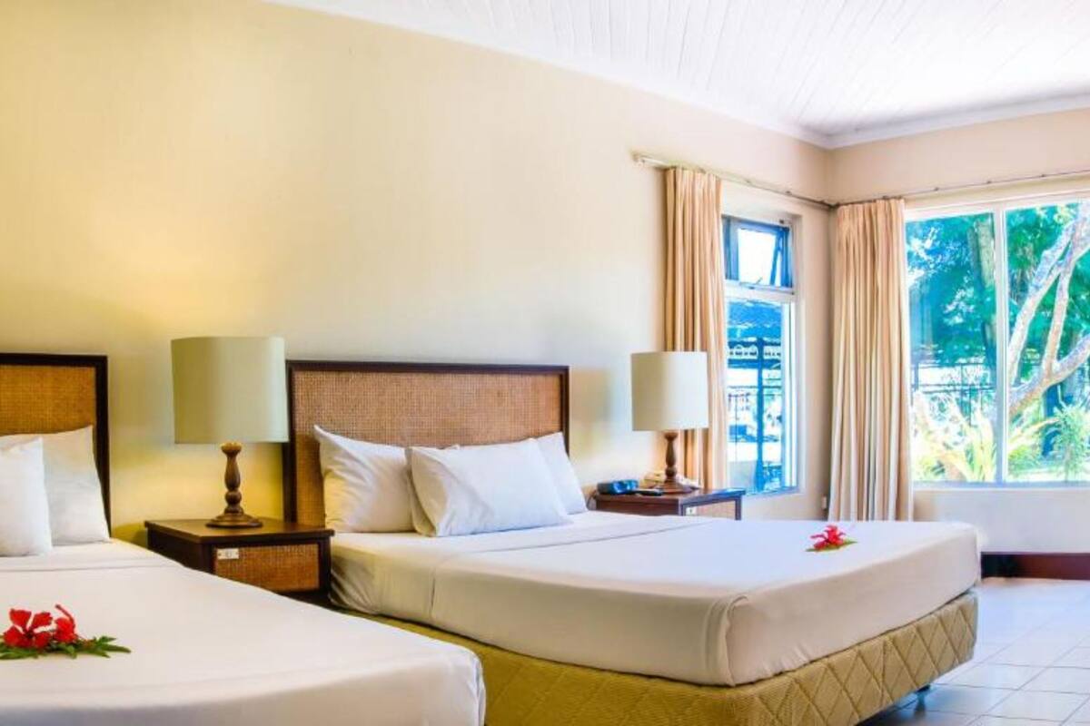 A hotel room with two beds, a large window with a view of trees, and a door leading outside.