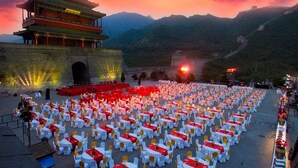 Un bâtiment traditionnel avec un toit rouge et des murs blancs, entouré d’un grand espace extérieur aménagé avec des tables et des chaises.