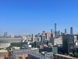 Un paisaje urbano con una mezcla de edificios modernos y tradicionales, un cielo azul despejado y un estadio grande al frente.