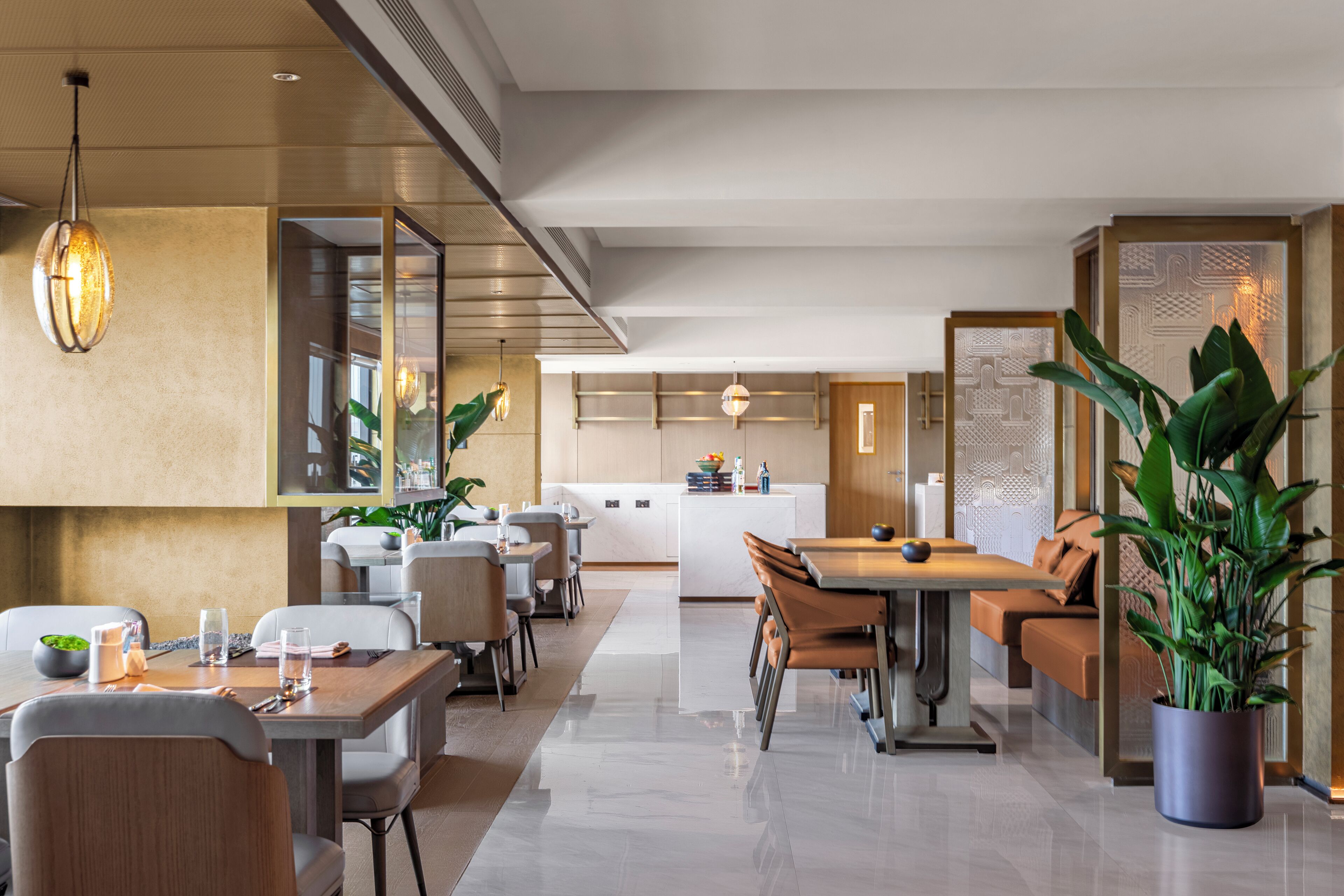 A modern hotel lobby with a dining area, a kitchen, and a seating area with a large plant.