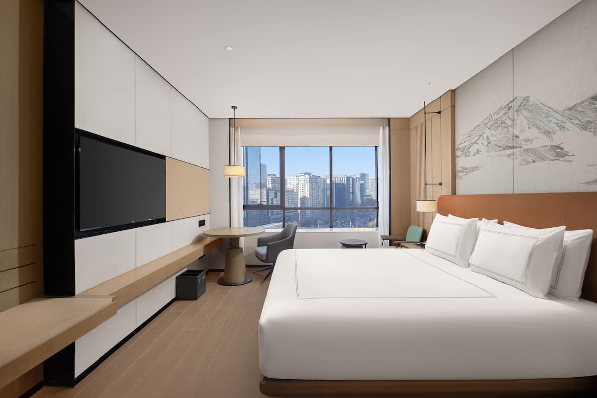 Ein modernes Hotelzimmer mit einem großen Bett, einem Flachbildfernseher, einem Schreibtisch und Blick auf die Stadt.