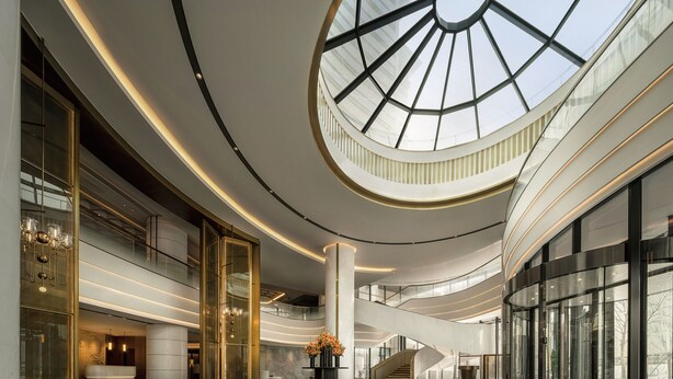 Un hall d’entrée spacieux avec un atrium central, un escalier et un grand plafond en verre.
