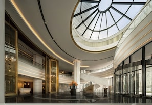Eine geräumige Lobby mit einem zentralen Atrium, einer Treppe und einer großen Glasdecke.
