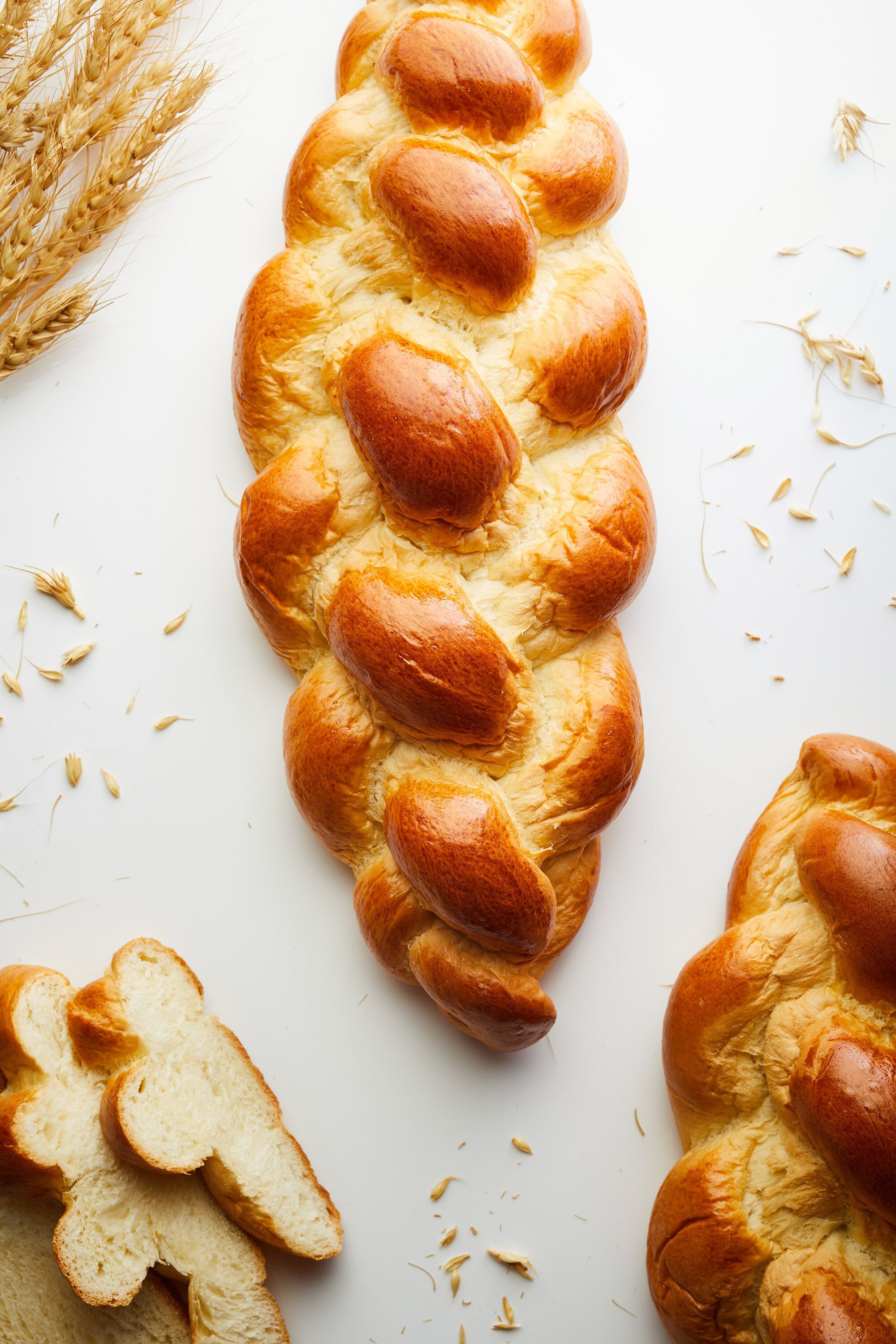 A braided loaf of bread with wheat stalks and scattered grains around it.