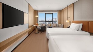 Une chambre d’hôtel avec deux lits, une télévision, un bureau avec une chaise, un canapé et une vue sur la ville.