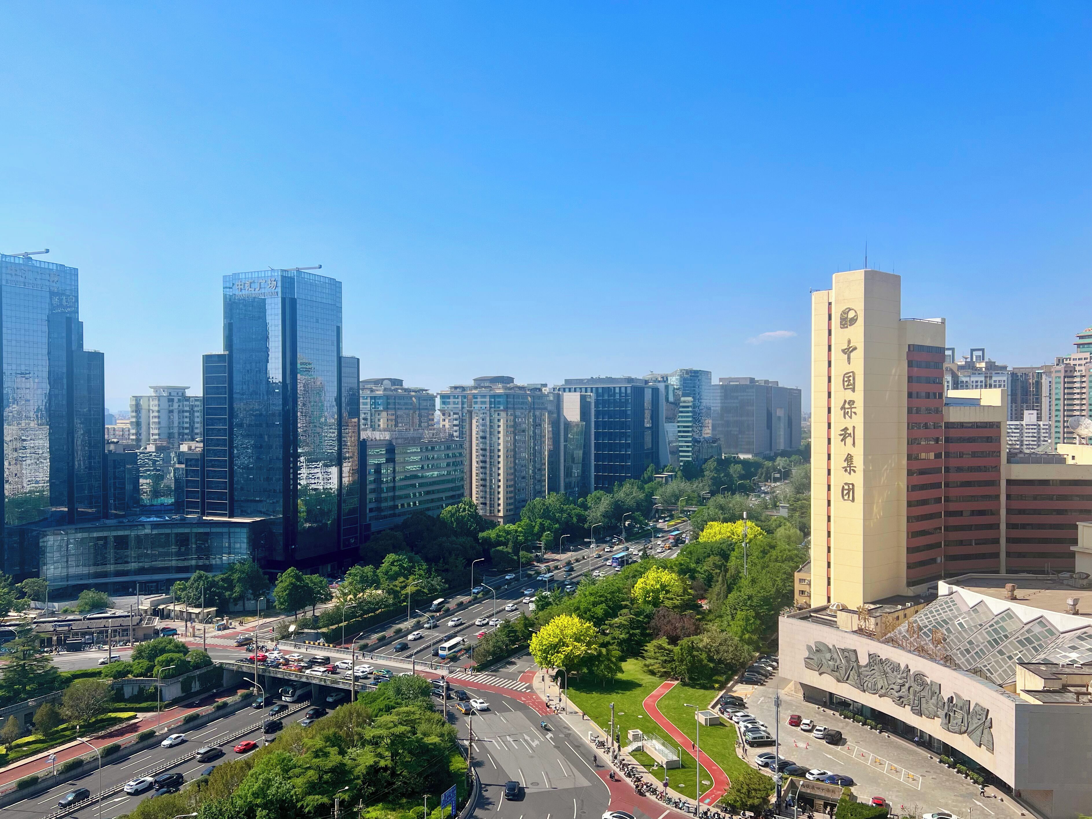 Un paisaje urbano con altos edificios modernos, una avenida central con vehículos y un edificio grande con señalización.
