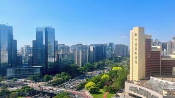 Un paisaje urbano con altos edificios modernos, una avenida central con vehículos y un edificio grande con señalización.