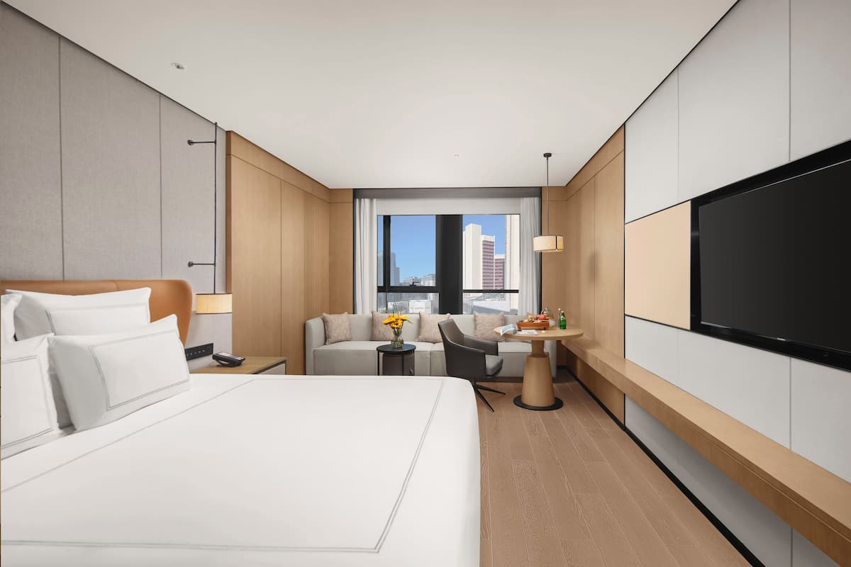Ein modernes Hotelzimmer mit einem großen Bett, einem Schreibtisch, einer Couch und einem Fernseher.