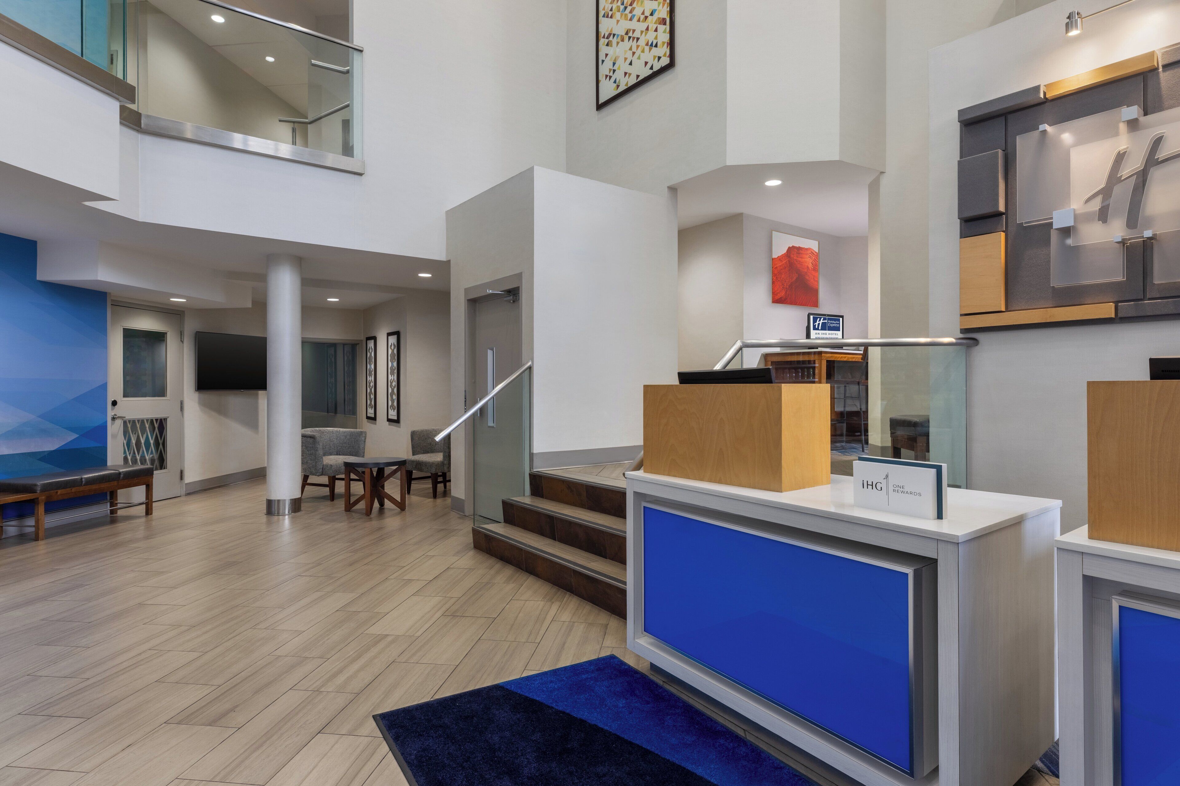 A modern hotel lobby with a reception desk, seating area, and a staircase leading to an upper level.