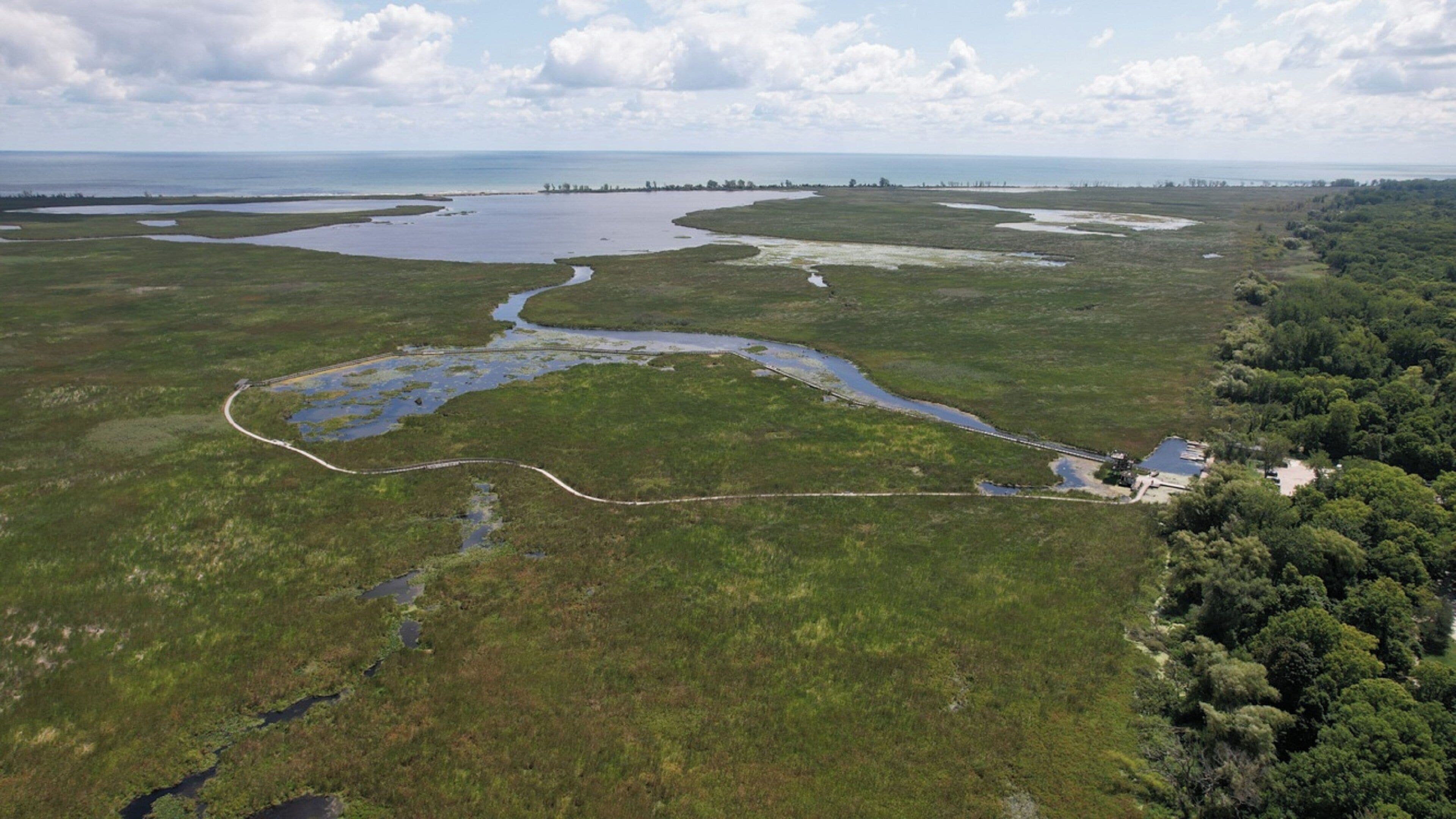An aerial view of a coastal landscape with water bodies, a winding road, and dense forest areas.