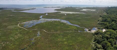 An aerial view of a coastal landscape with water bodies, a winding road, and dense forest areas.