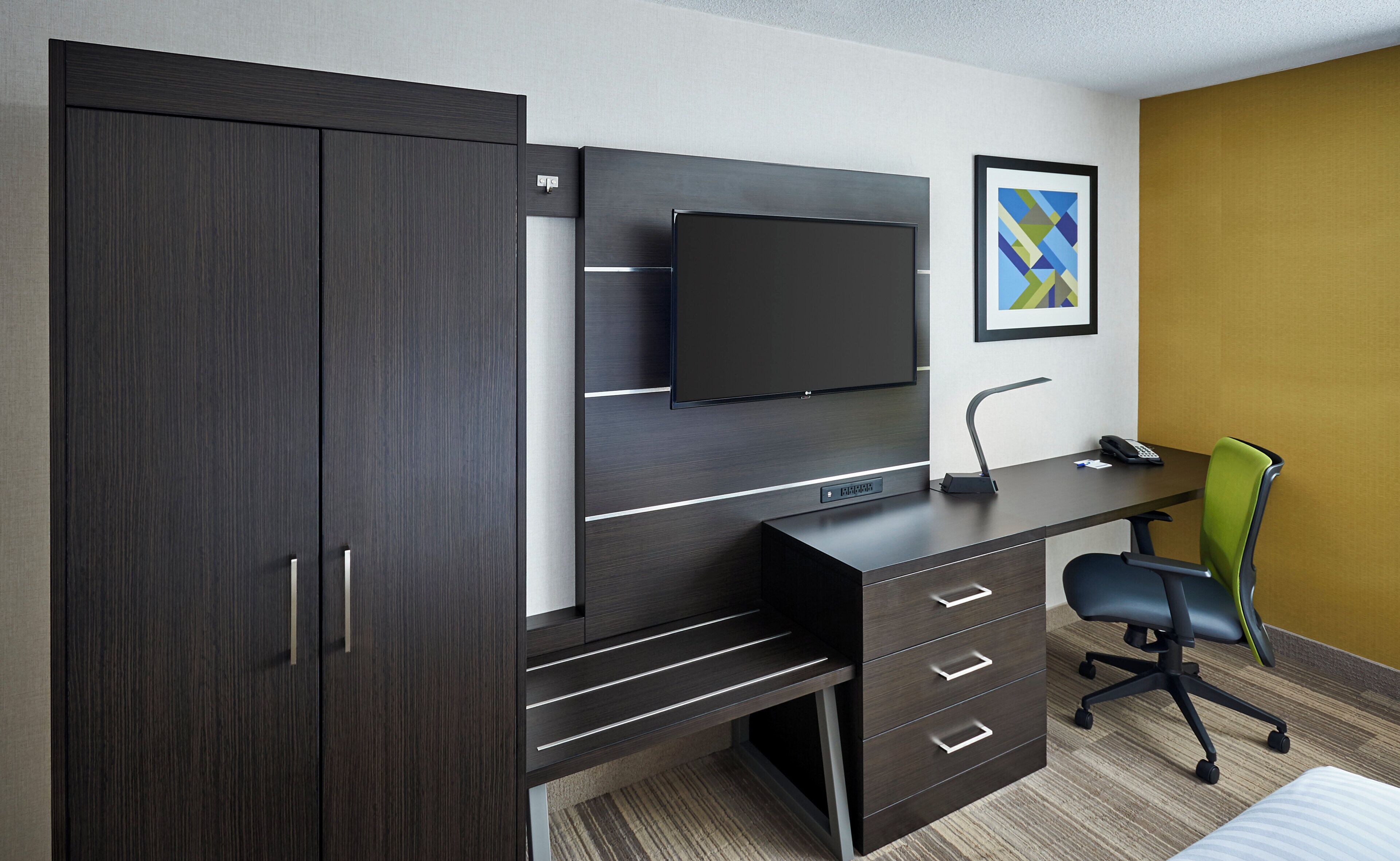 A modern office space with a dark wood desk, a flat-screen monitor, a telephone, and a green office chair.