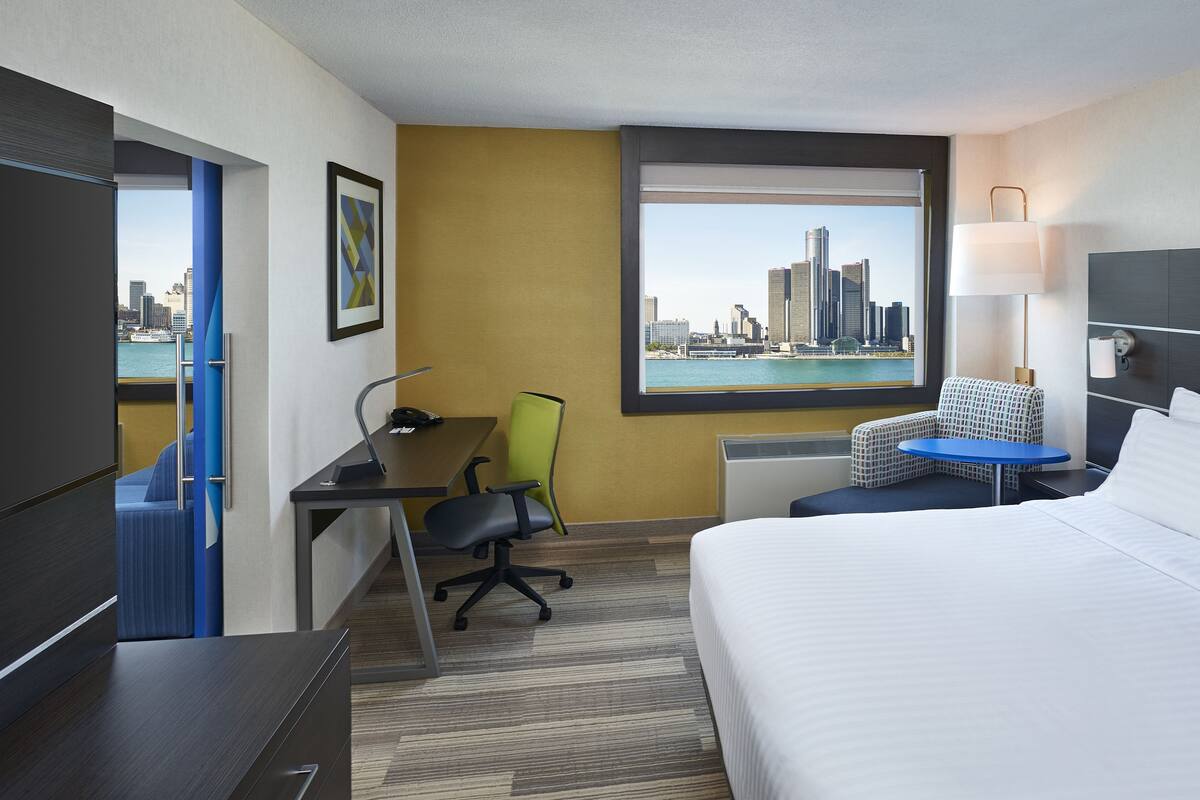 Une chambre d’hôtel équipée d’un lit, d’un bureau, d ’une chaise et offrant une vue sur le paysage urbain à travers une grande fenêtre.