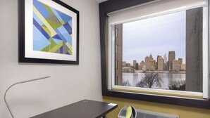 A hotel room with a desk, chair, framed artwork, and a window with a cityscape view. - Holiday Inn Express Windsor Waterfront by IHG (Windsor)