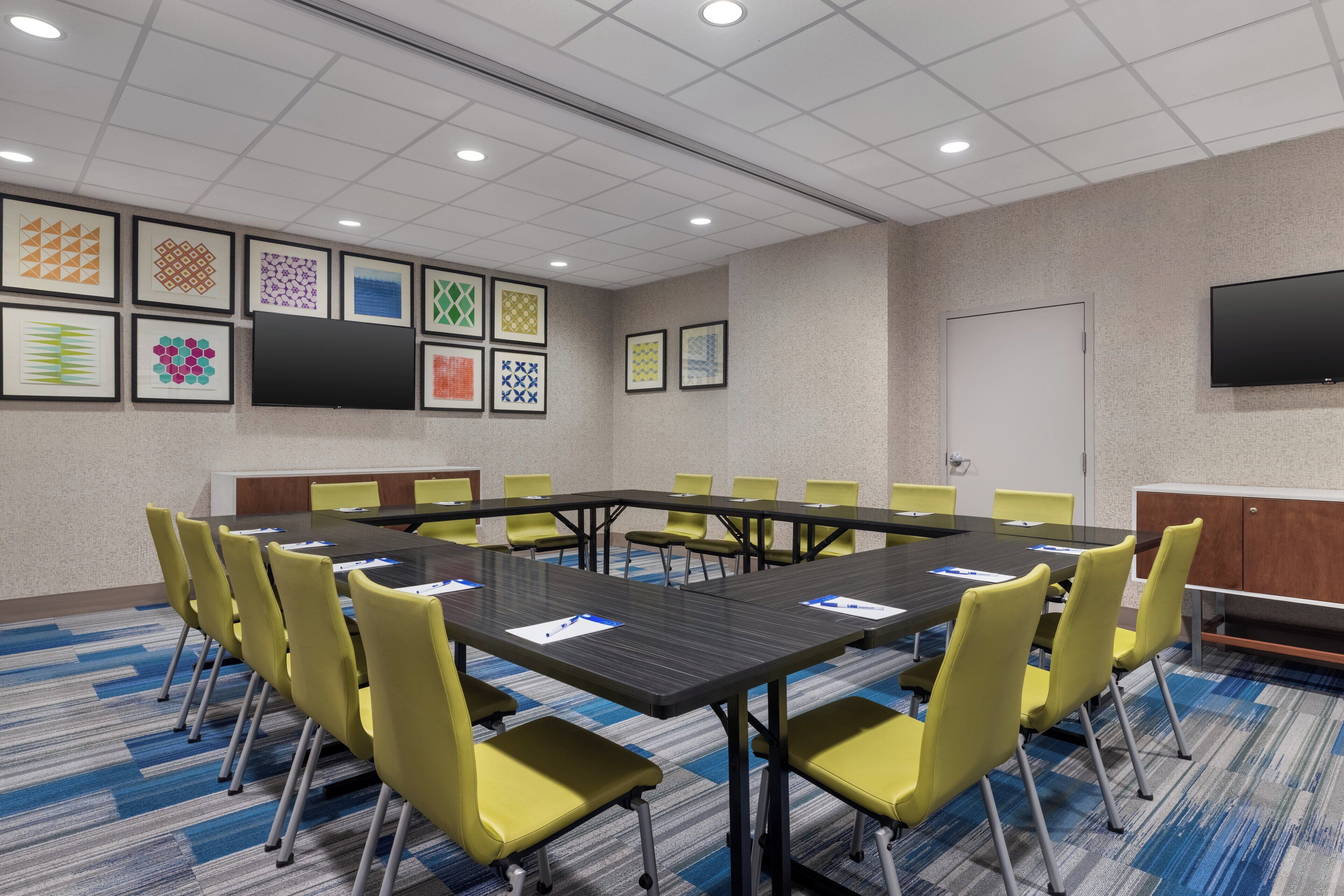 A conference room with a long table, yellow chairs, and framed artwork on the walls.