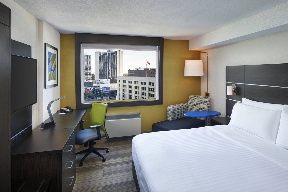 Une chambre d’hôtel équipée d’un lit, d’un bureau, d’une chaise et d’une fenêtre donnant sur la ville.