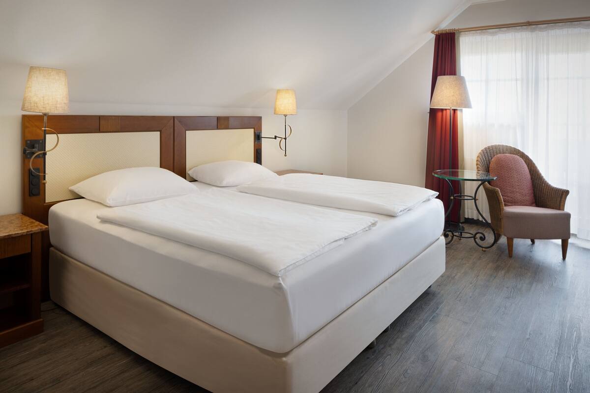 Une chambre d’hôtel avec un grand lit, deux tables de chevet, une chaise et une petite table avec une lampe.
