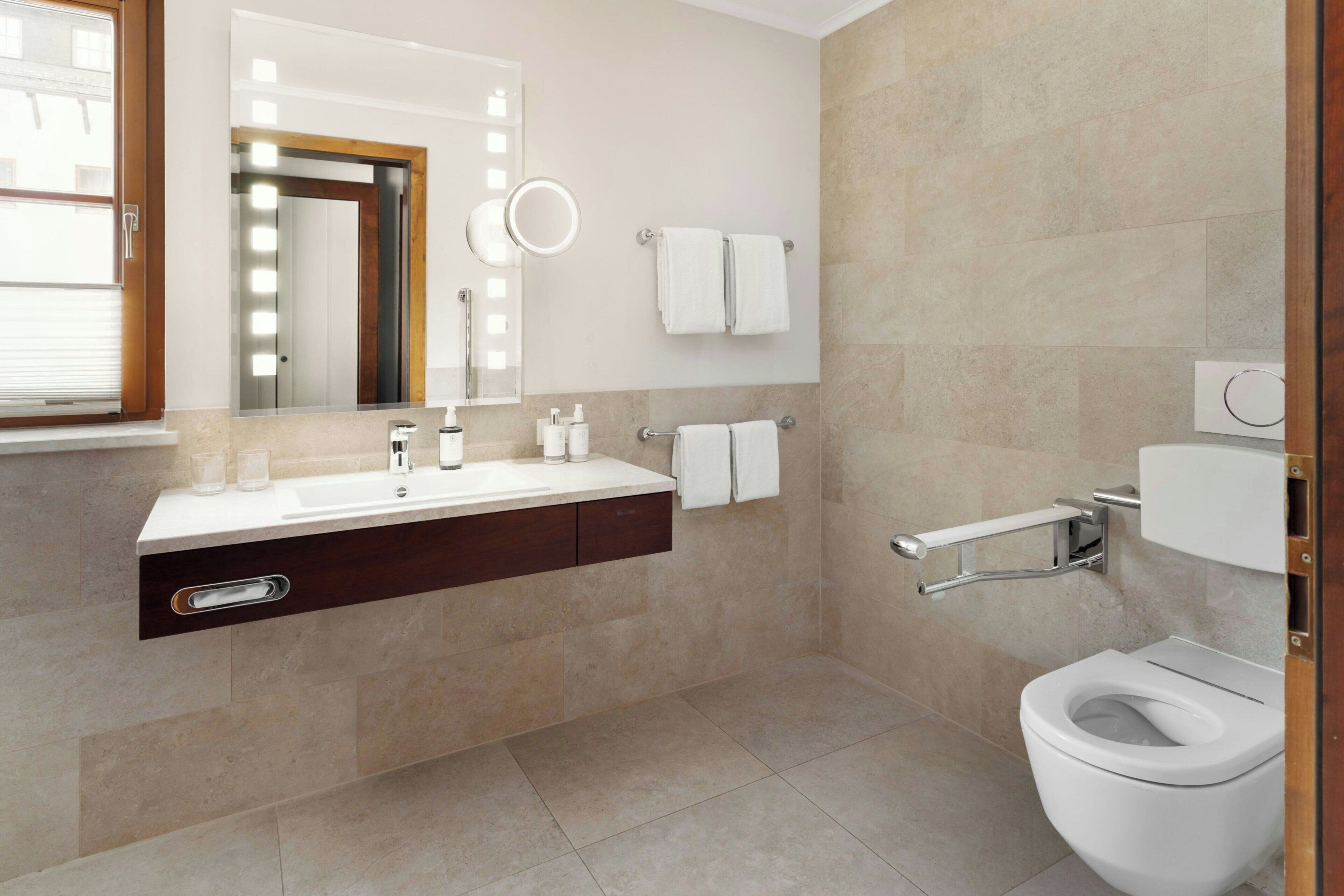Une salle de bain moderne équipée d’un lavabo, d’un miroir, d’un porte-serviettes et de toilettes.
