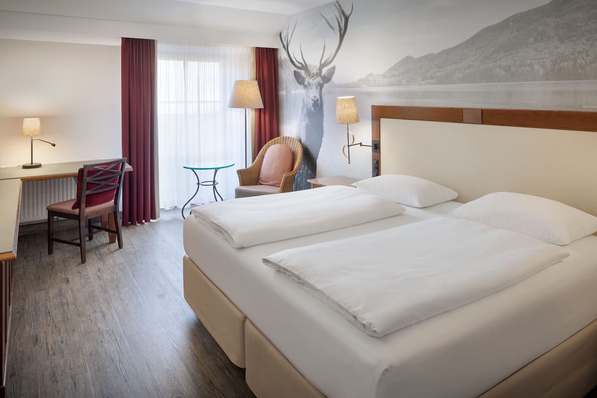 Une chambre d’hôtel avec deux lits, un bureau, une chaise, une lampe et une grande fresque murale.