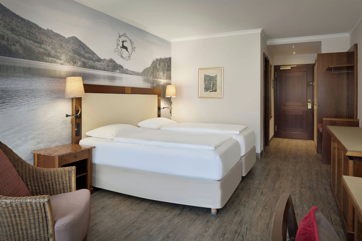 Une chambre d’hôtel avec un lit, deux tables de chevet avec des lampes, une chaise, un plancher en bois et un tableau au mur.