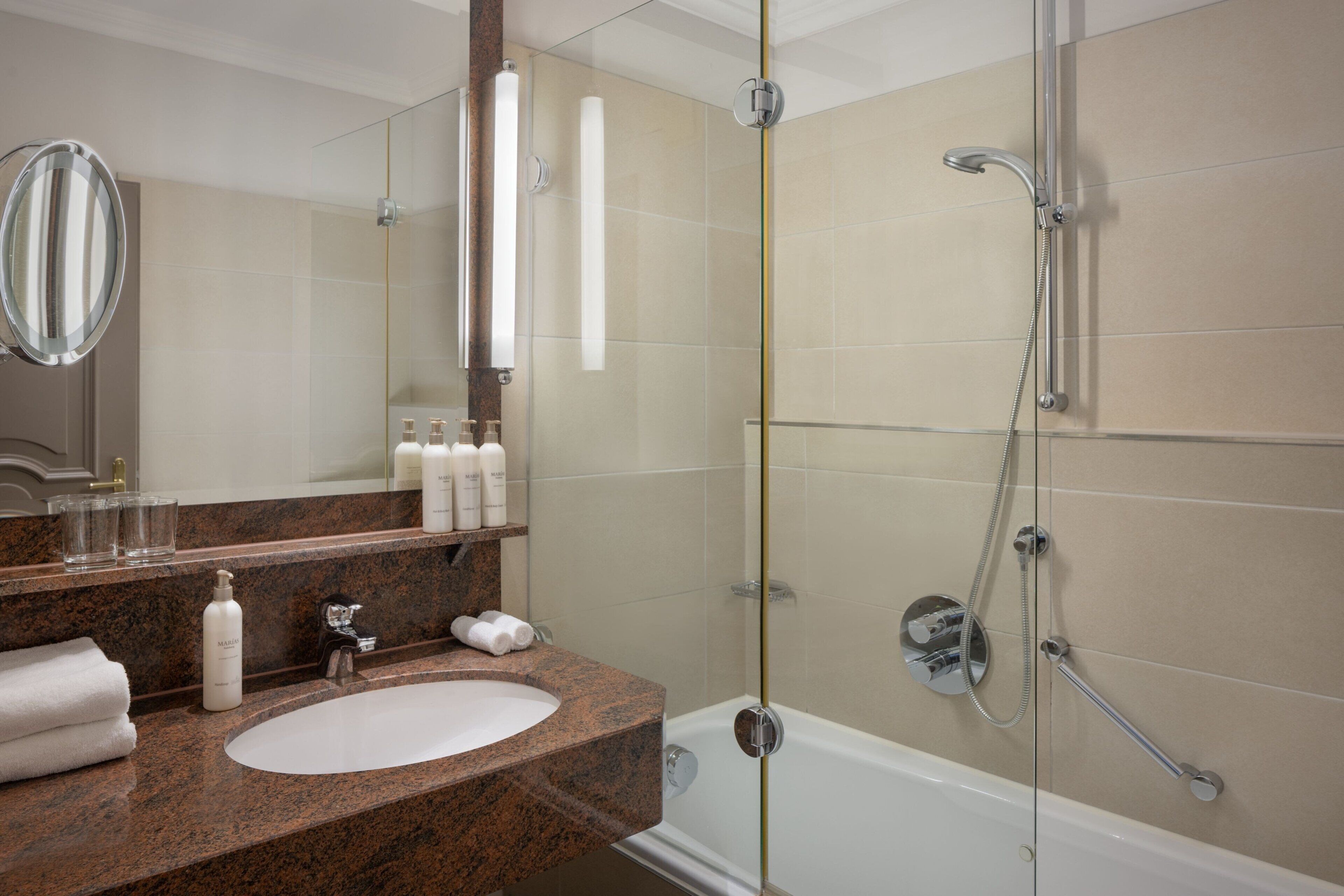 A modern bathroom with a granite countertop sink, a large mirror, and a glass-enclosed shower area.