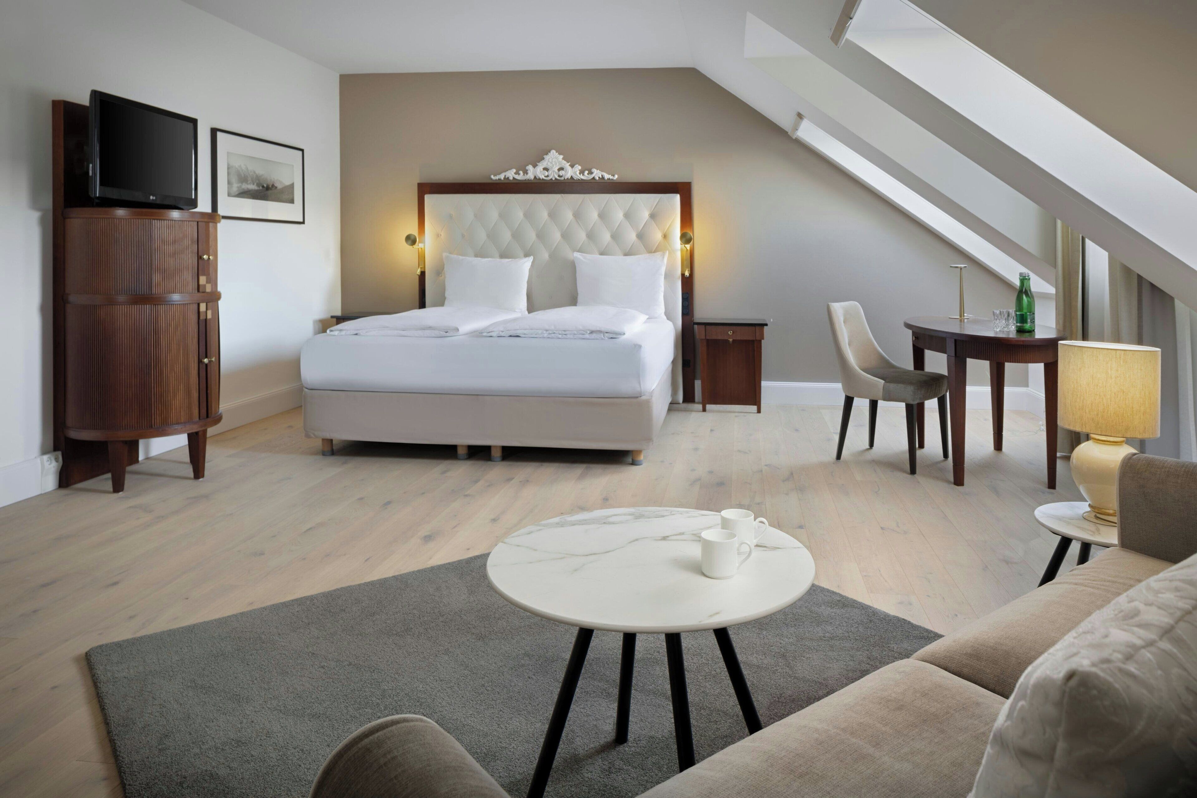 Quarto de hotel com uma cama grande, televisão, escrivaninha com luminária e uma cadeira.