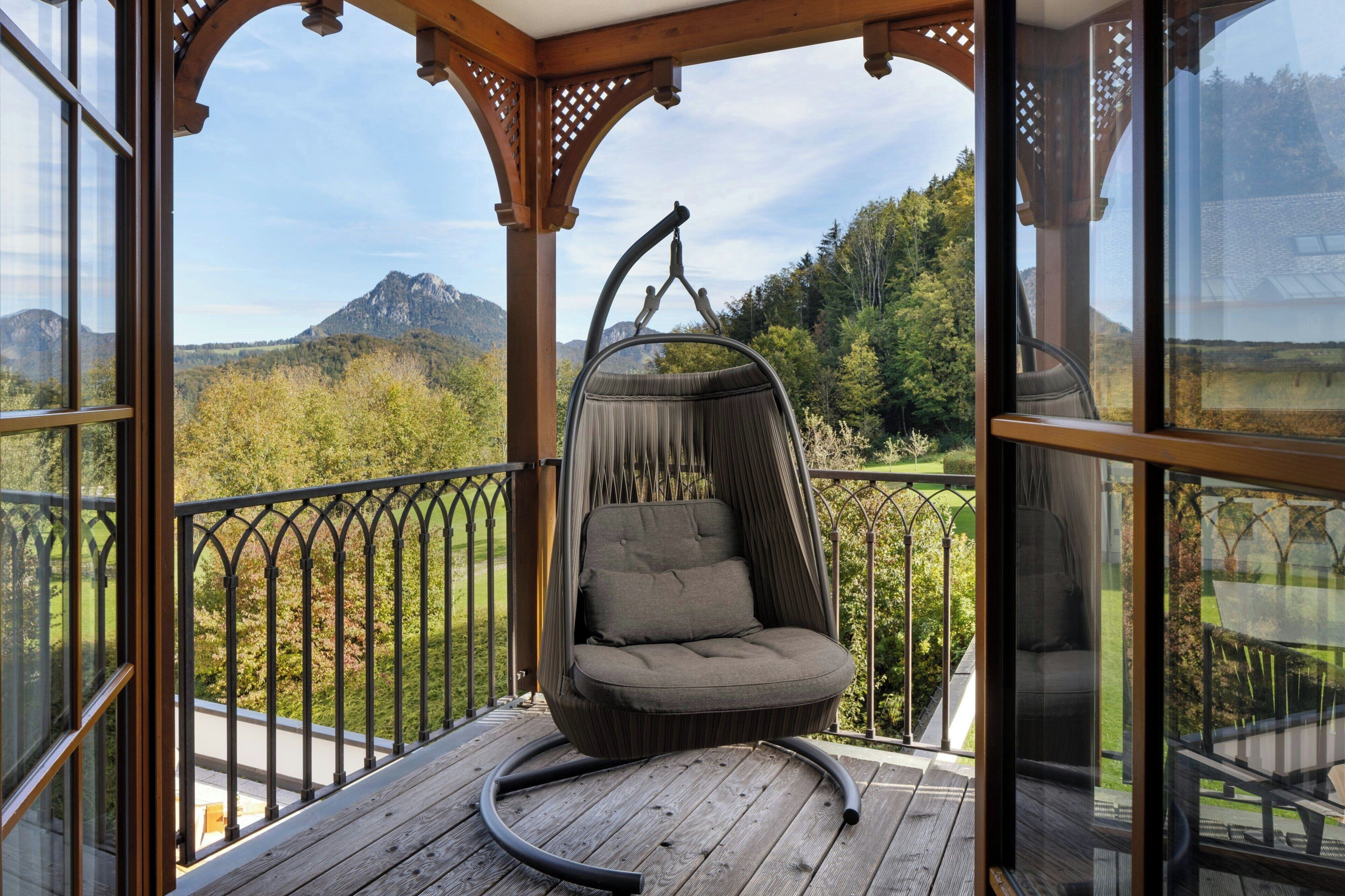 Une terrasse en bois avec un fauteuil suspendu donnant sur un paysage montagneux.