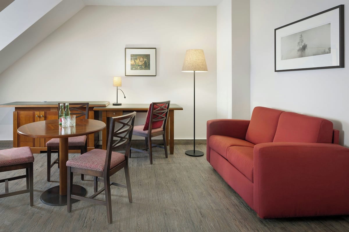 Un salon moderne avec une table ronde en bois, deux chaises, un canapé rouge et un lampadaire.