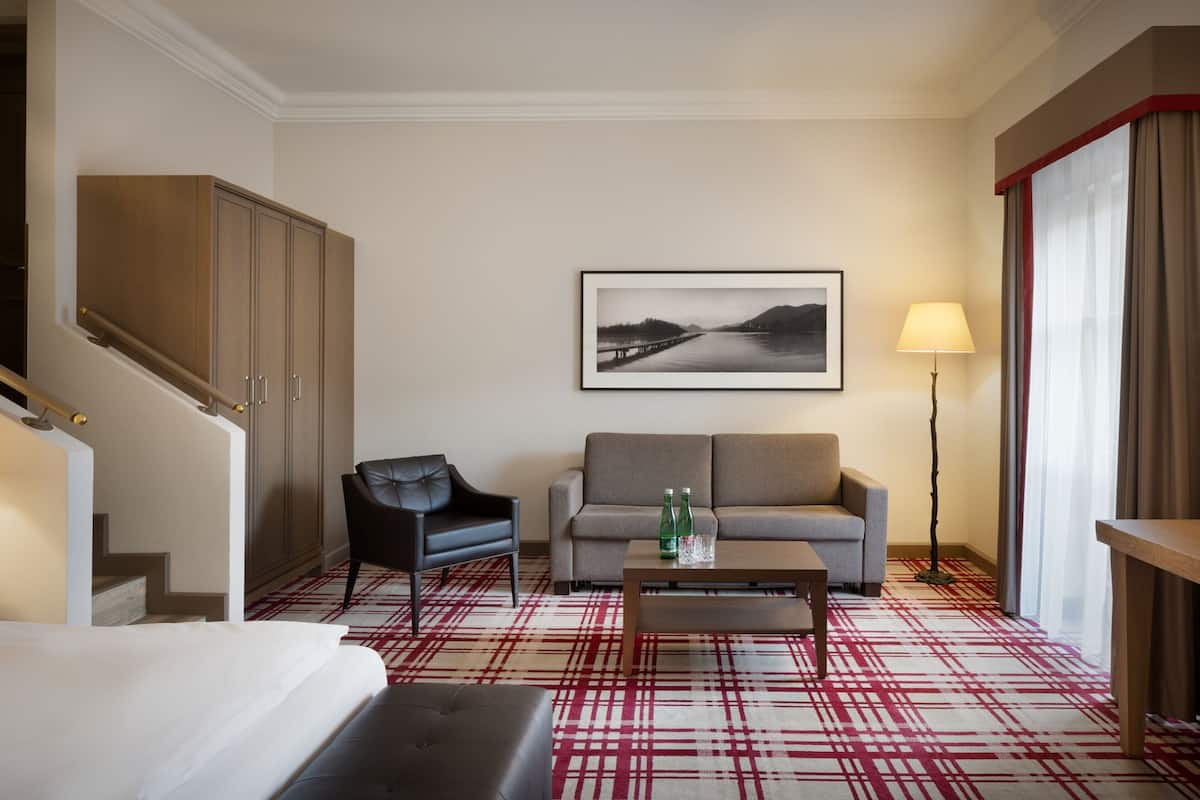 Une chambre d’hôtel comprenant un canapé, un fauteuil, une table basse, un lit, un escalier et un tableau encadré au mur.