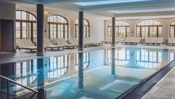 A large indoor swimming pool with lounge chairs and large arched windows.