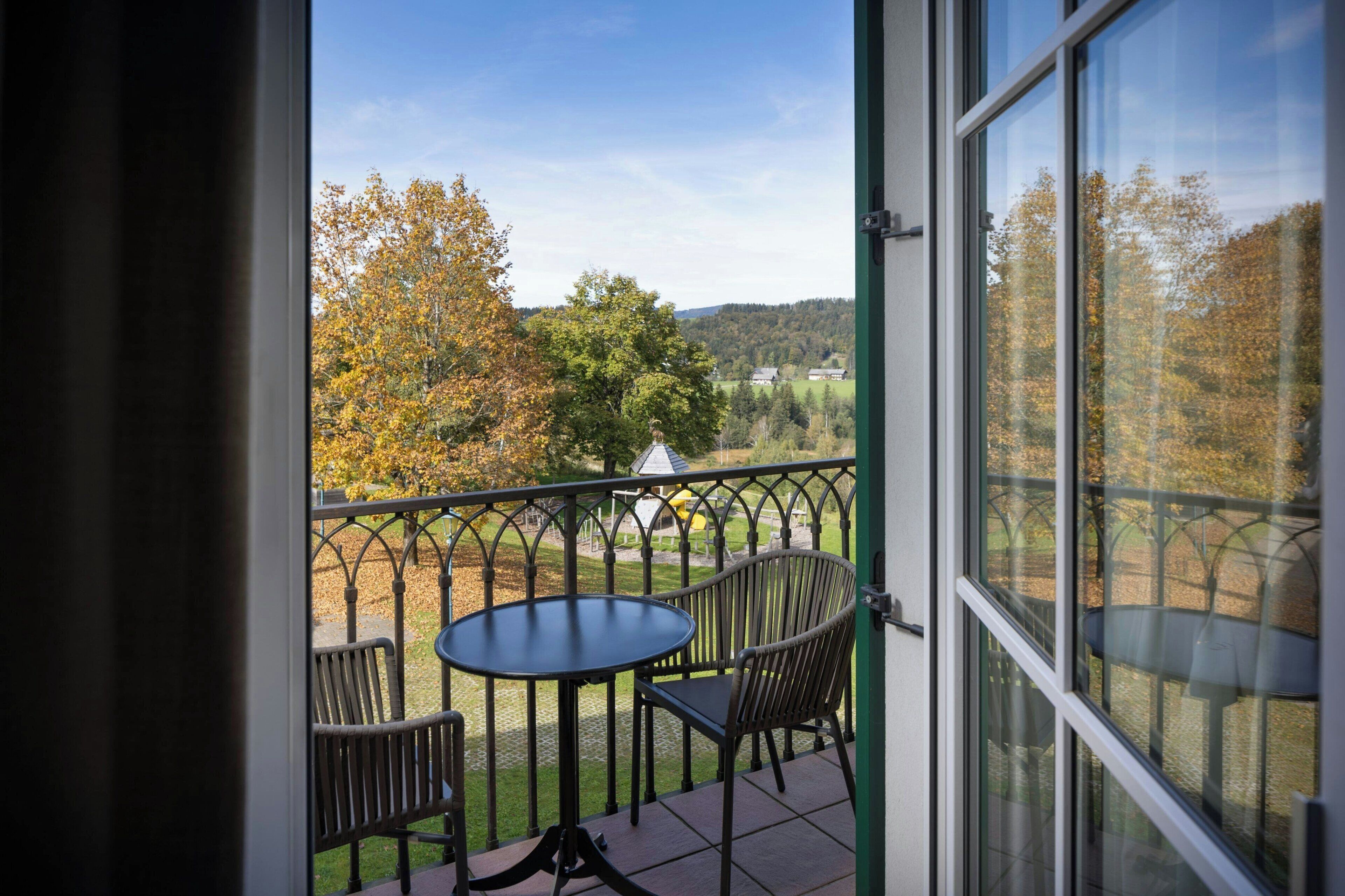 A balcony with a table and chairs, offering a view of trees and a distant landscape.
