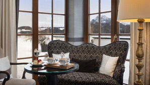 A cozy room with a patterned sofa, a glass table with a tray of food and drinks, and large windows offering a view of a snowy landscape.