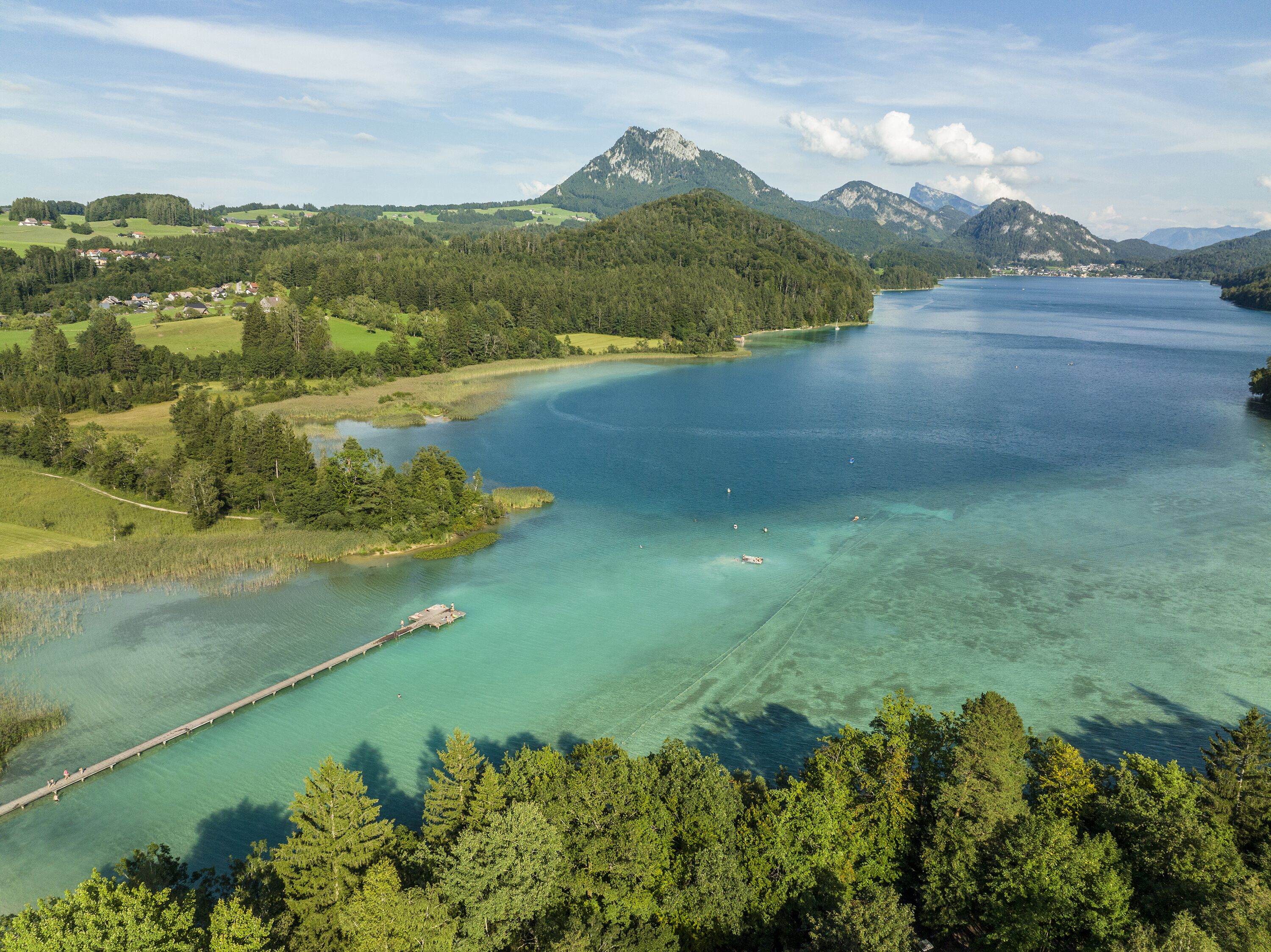 A lake surrounded by forested hills and a small dock extending into the water.