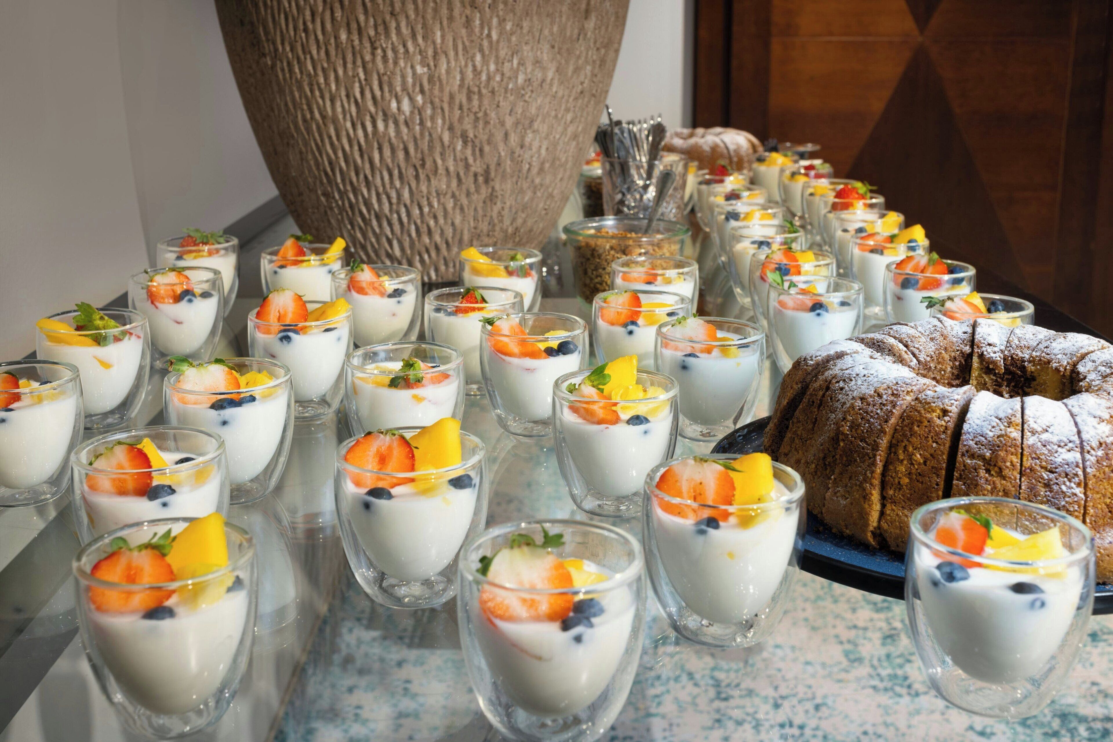 A buffet table with fruit-topped yogurt cups and a loaf of bread.