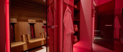 A sauna room with wooden benches and a glass door leading to a shower area with a red-lit ambiance.