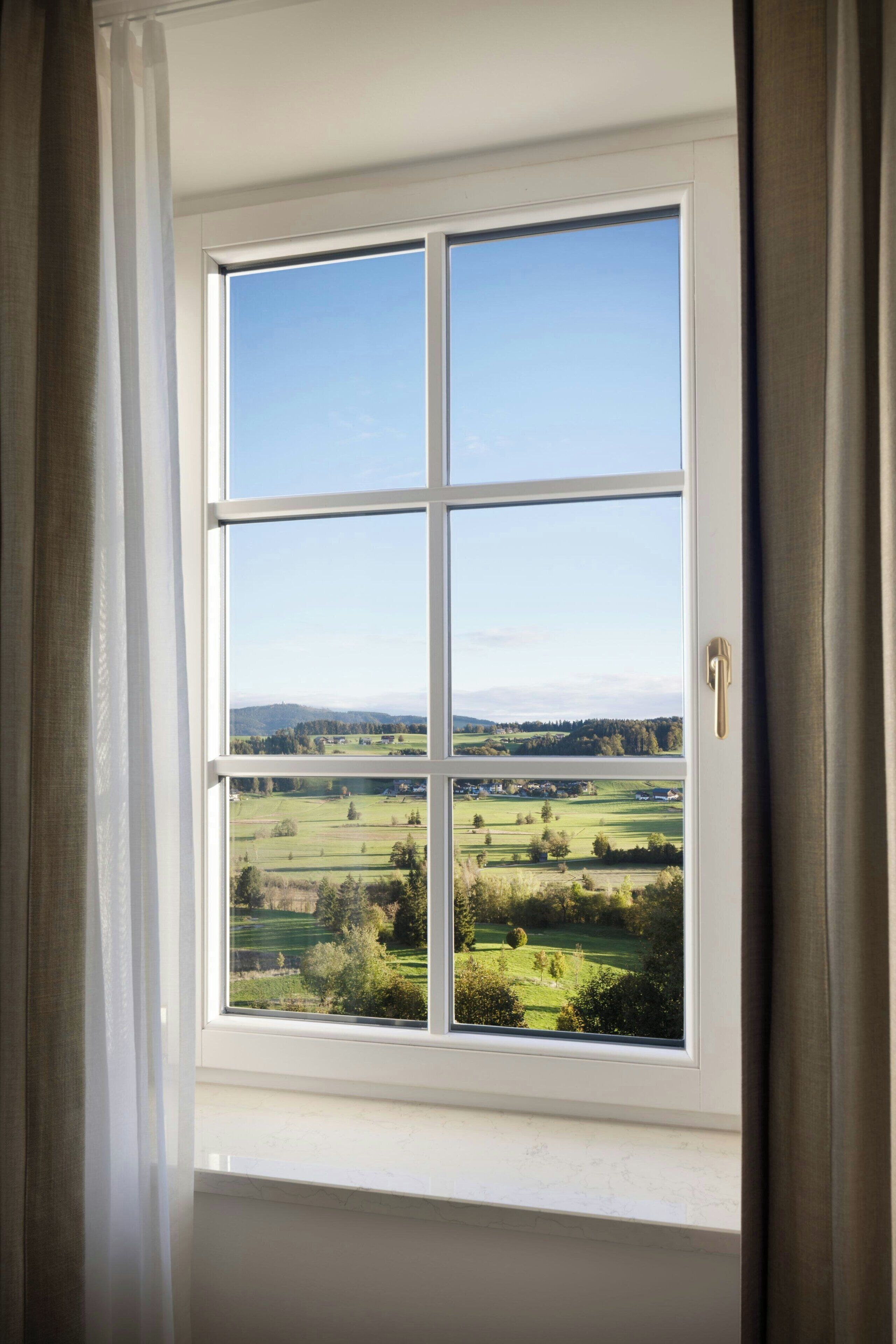 Una ventana que ofrece vistas despejadas de un paisaje verde, con campos y colinas lejanas.