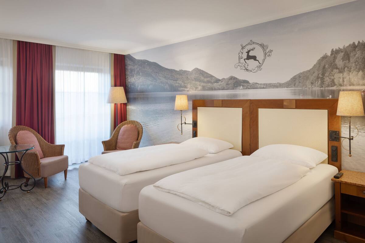 Une chambre d’hôtel avec deux lits, une vue sur un lac et une fresque représentant un cerf sur le mur.