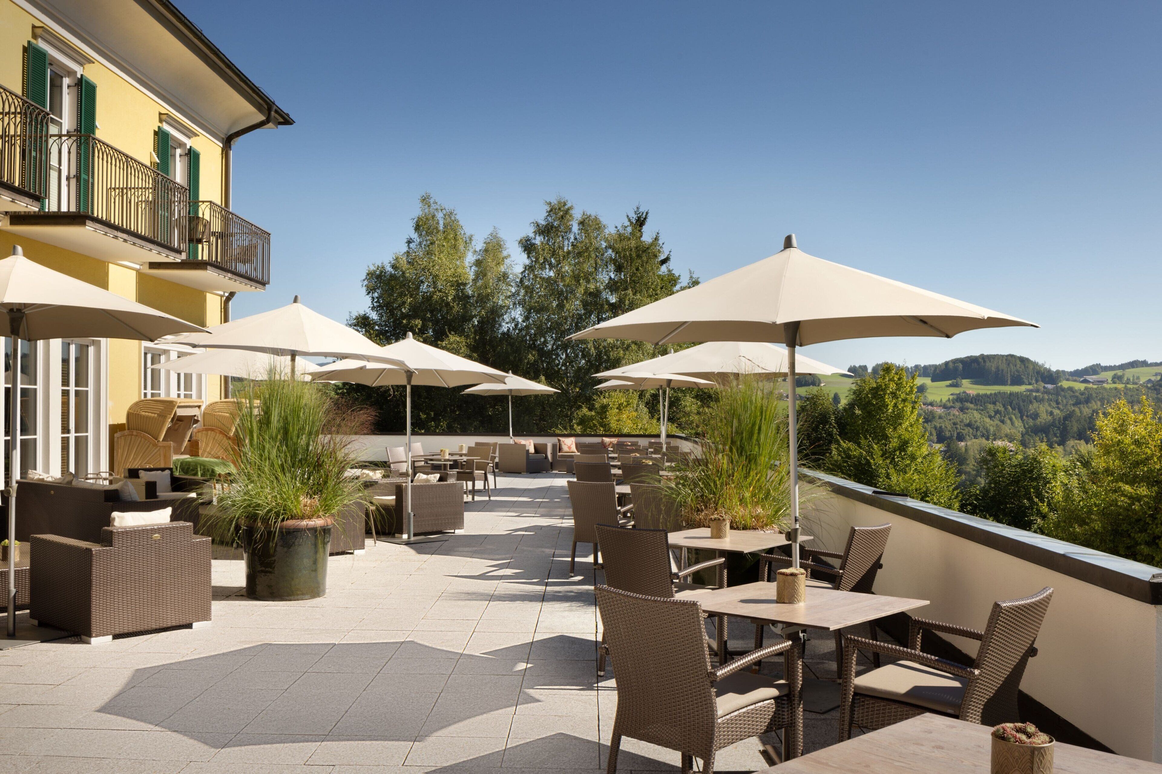 Eine Außenpatio mit Korbmöbeln, beigefarbenen Sonnenschirmen und Blick auf die Landschaft.