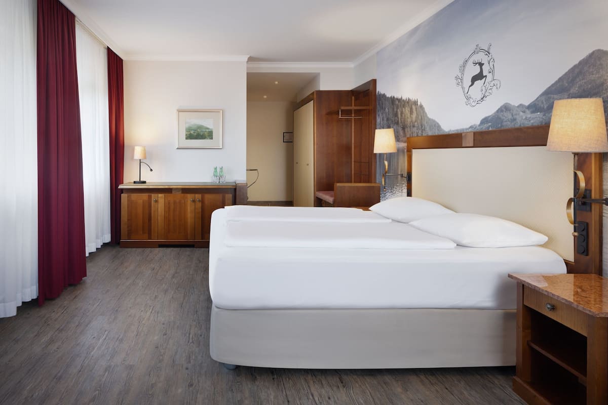 Une chambre d’hôtel avec un grand lit, une commode en bois, un bureau et un tableau accroché au mur.