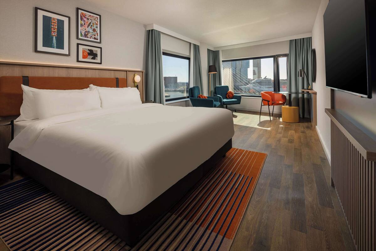 A hotel room with a large bed, a desk, a chair, and a TV.