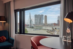 A hotel room with a large window offering a view of a bridge and city buildings.