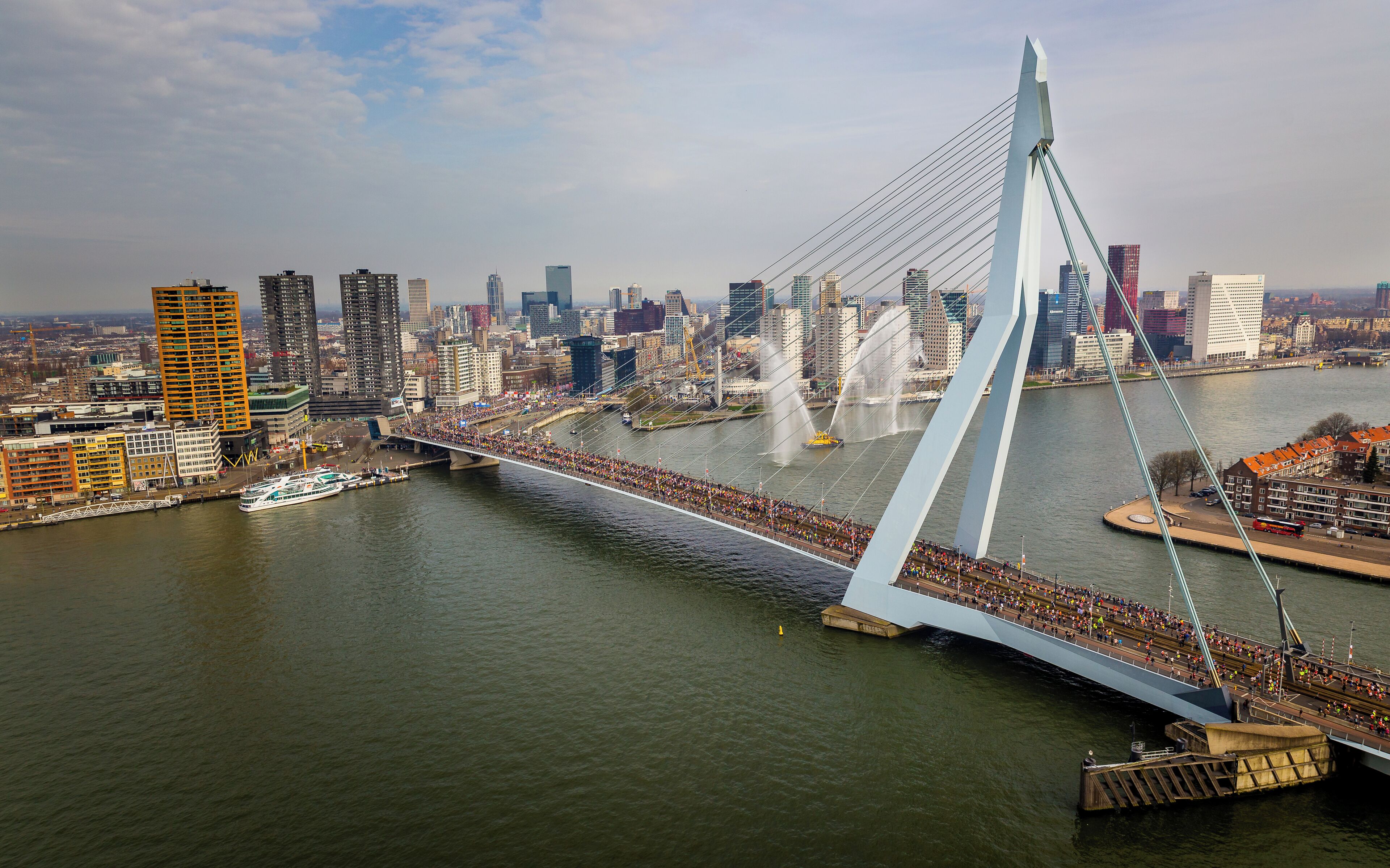 Un puente moderno con un paso peatonal sobre un río, rodeado por un paisaje urbano con diversos edificios.