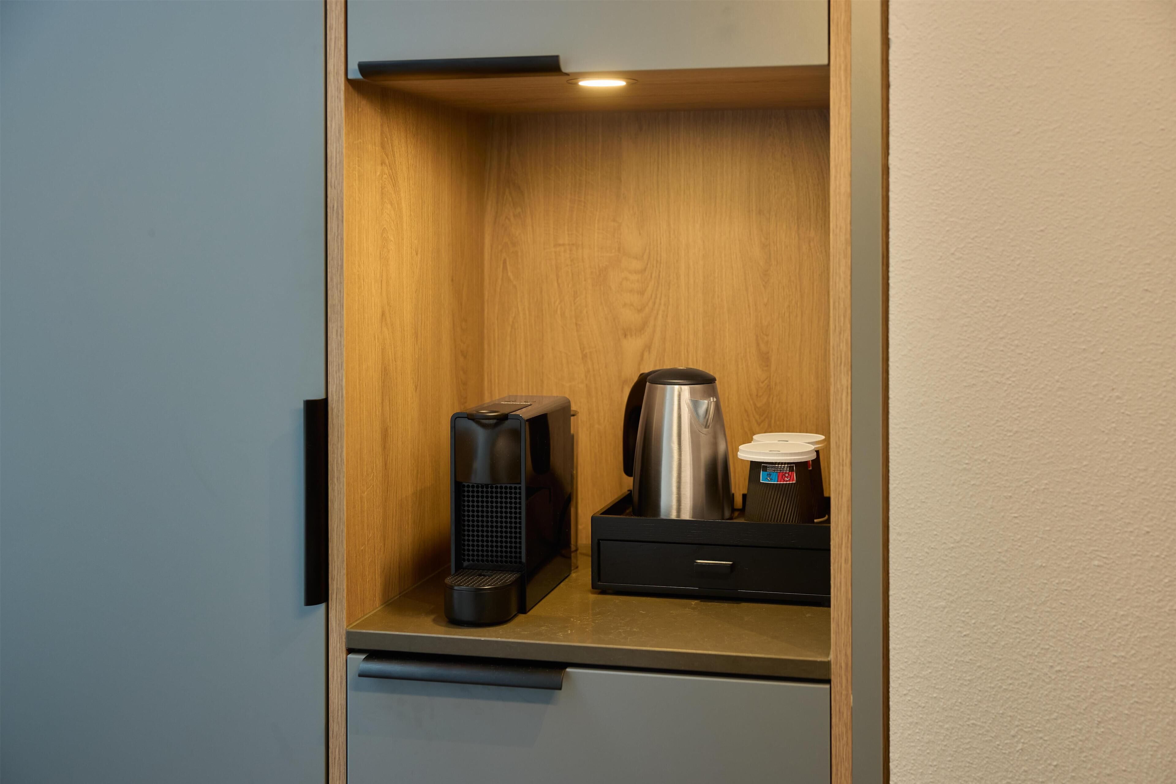 Un angolo cottura compatto con macchina da caffè, bollitore e un piccolo cassetto.