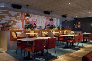 A restaurant with round tables, red chairs, and a colorful abstract mural on the wall.